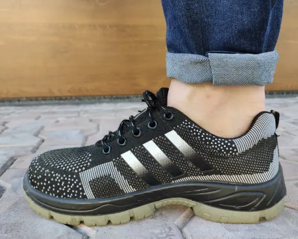 Czarne buty sportowe z białymi paskami i podwiniętymi nogawkami jeansów. Idealny przykład, jak podwinąć spodnie.