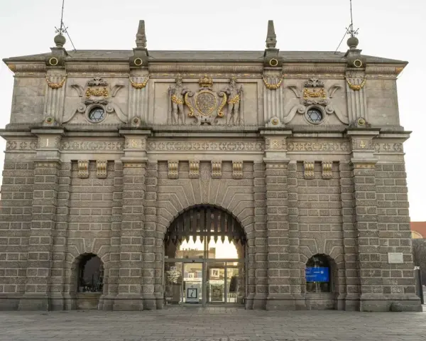 Majestatyczna Brama Wyżynna w Gdańsku, ozdobiona herbem i rzeźbami, zaprasza do zwiedzania.