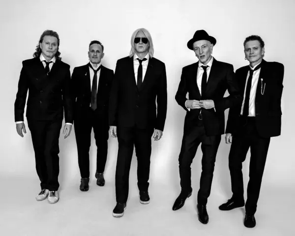 Fünf Männer in schwarzen Anzügen und Krawatten, die wie der titel von Def Leppard aussehen, posieren für ein Schwarz-Weiß-Foto.