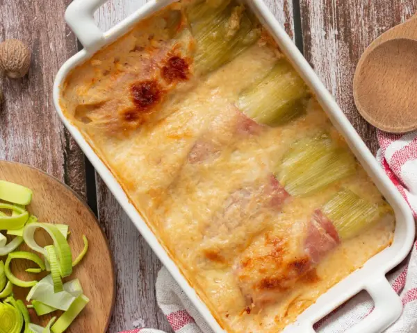 Gratin de poireaux au jambon, doré et crémeux, prêt à être dégusté. Une recette réconfortante.