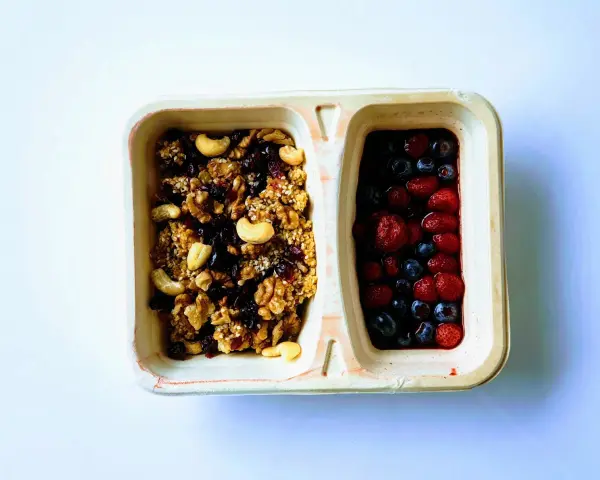Dwie przegródki pojemnika: jedna z granolą i orzechami, druga z jagodami i truskawkami. Czy kasza jaglana ma gluten? Ta granola wygląda na bezglutenową!