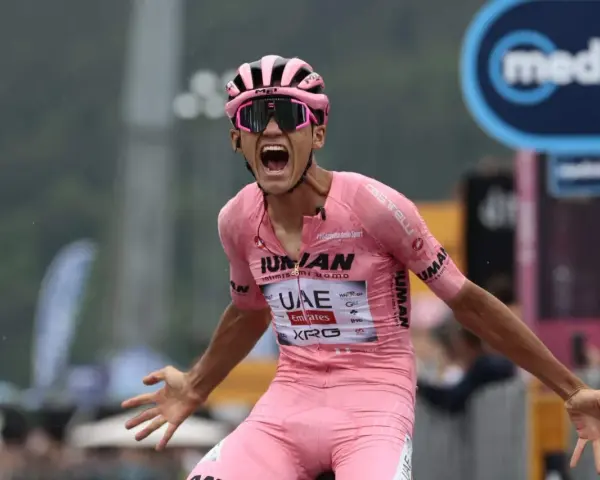 Isaac Del Toro, a cyclist in a pink jersey, screams in triumph, arms outstretched.