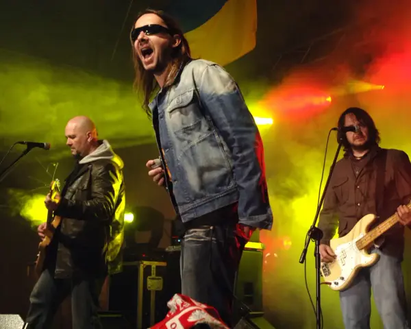 Energetyczne kapele punkowe z lat 80. na scenie, w dymie i kolorowych światłach. Wokalista krzyczy do mikrofonu, gitarzysta gra na basie.