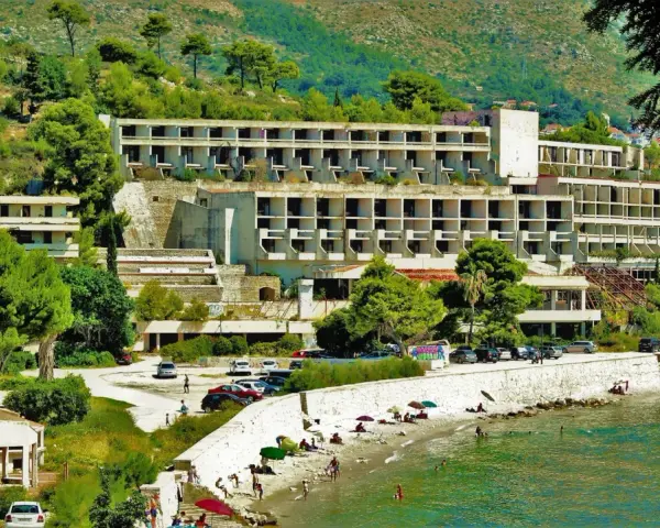 Opuszczone hotele Chorwacja, zniszczone budynki hotelowe na wzgórzu, plaża z ludźmi i morze.