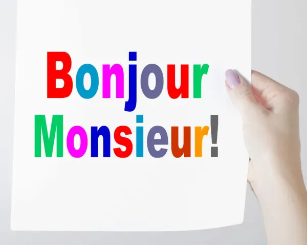 Una mano sostiene un cartel con "Bonjour Monsieur!" escrito en letras de colores.