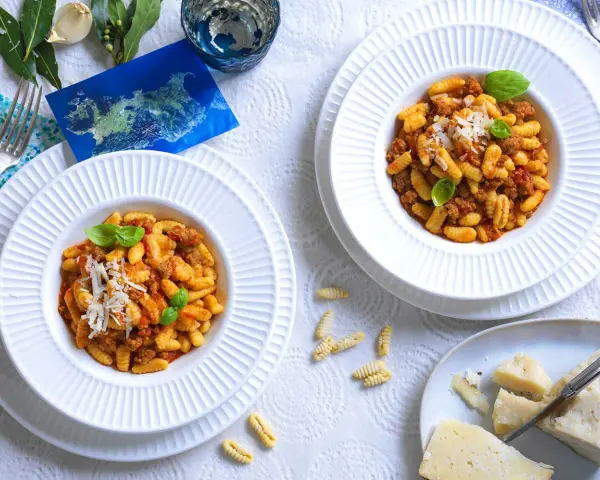 Due piatti di gnocchetti alla campidanese, un assaggio di Sardegna con sugo di salsiccia e pomodoro, guarniti con basilico e parmigiano.