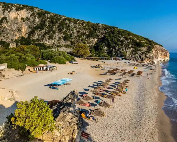Piękne albania plaże z rzędami parasoli i leżaków, skaliste zbocze i turkusowe morze.