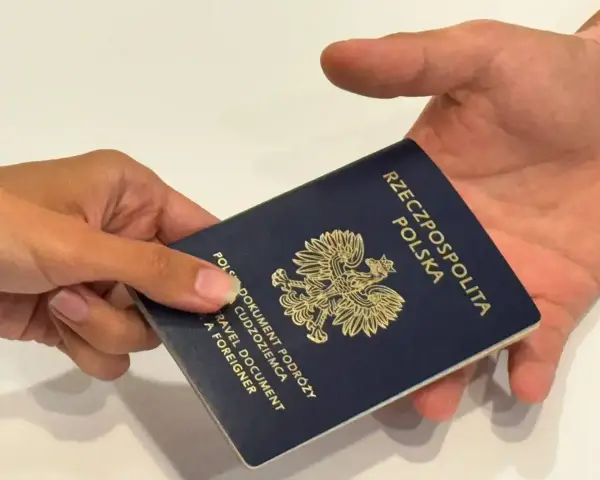 Dłoń przekazuje ciemnoniebieski paszport polski z godłem orła. Dokument podróży gotowy do przekroczenia granicy.