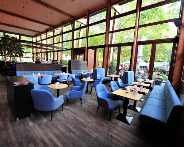Gemütliches **Cafe Wilmersdorf** mit blauen Sesseln und Bänken, Holzboden und großen Fenstern, die auf eine grüne Terrasse blicken.