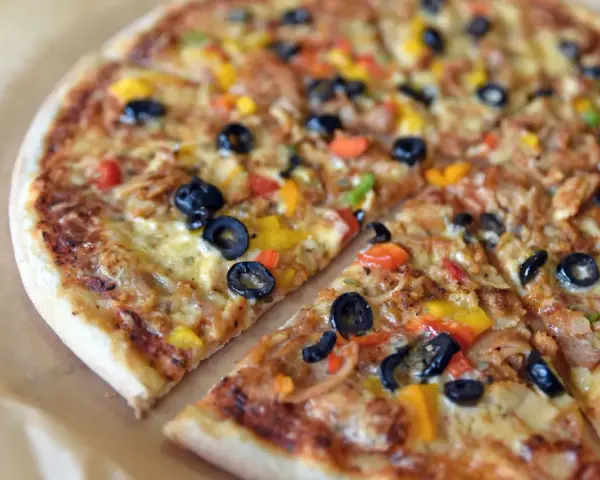 Co to jest pizza? To pyszna, okrągła pizza z oliwkami, papryką i serem, pokrojona na kawałki.