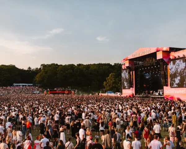 Tłum ludzi na festiwalu Bittersweet 2026, podziwiający scenę z wielkim ekranem i artystami. Słońce zachodzi, tworząc ciepłą atmosferę.