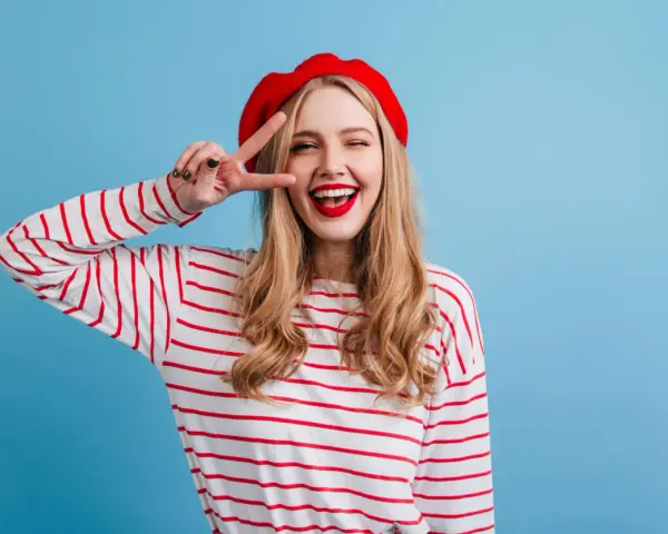 Mujer con boina roja y camiseta a rayas, haciendo el signo de la paz, con un estilo que evoca un caracter francés.