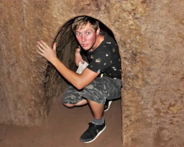 Młody mężczyzna kuca w wąskim tunelu, jednym z historycznych Cu Chi Tunnels.