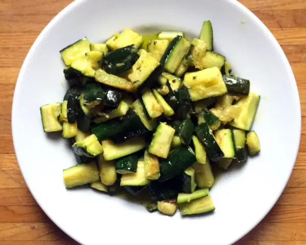 Zucchine in umido, un contorno saporito e leggero, servito in un piatto bianco su un tagliere di legno.
