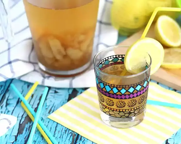 Ett glas med en färgglad dekorativ kant, fyllt med iste och en citronskiva. Bredvid står en karaff med iste och färska citroner. Perfekt iste recept för en varm dag.