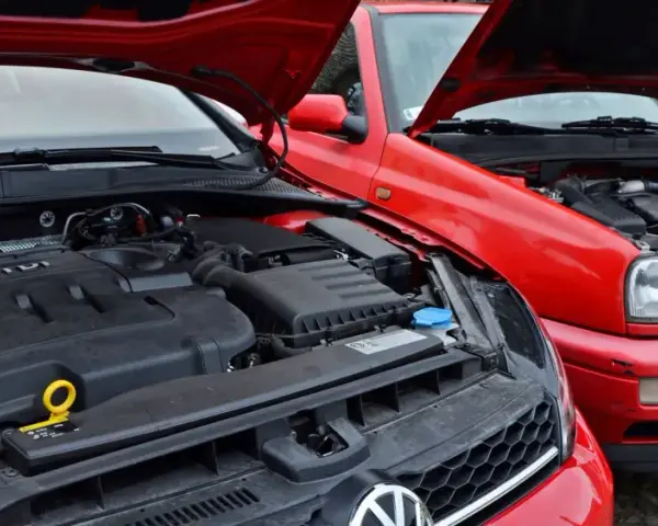 Dwa czerwone Volkswageny z otwartymi maskami. Nowszy model z silnikiem TDI obok starszego, gdzie widać stary diesel.