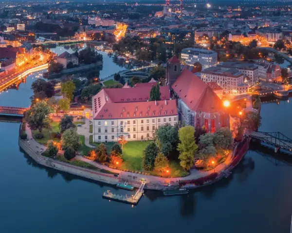 Ostrów Tumski we Wrocławiu nocą, z oświetlonymi budynkami i rzeką. To jedno z najpiękniejszych miejsc Wrocławia.