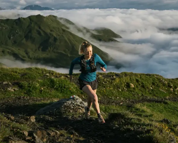 Donna corre su sentiero montano, immersa nella nebbia. Il trail running significato è libertà e sfida.
