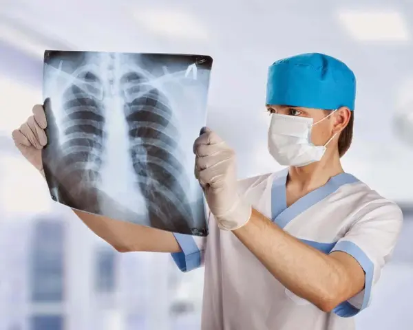 Un radiologo con mascherina e guanti esamina una radiografia del torace, analizzando attentamente ogni dettaglio per una diagnosi accurata.