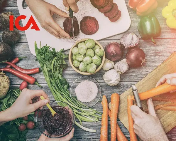ICA-logotypen över en bild av färska grönsaker som förbereds för ett recept. Rödbetor skivas, morötter skalas och en skål med puré.