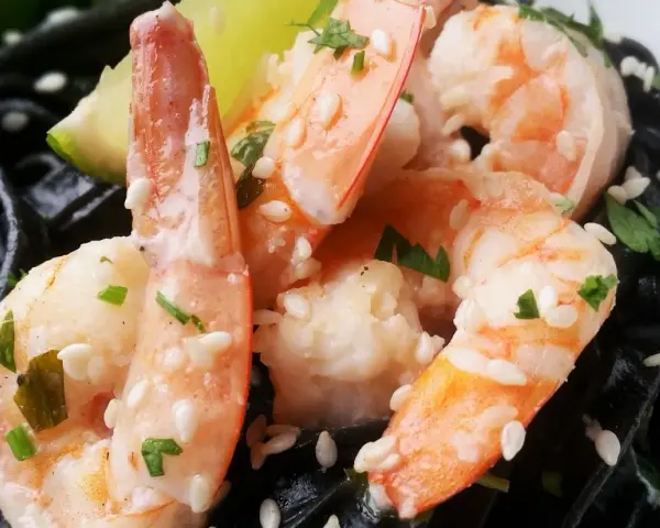 Krewetki z czarnym makaronem, posypane sezamem i natką pietruszki, z kawałkiem limonki.
