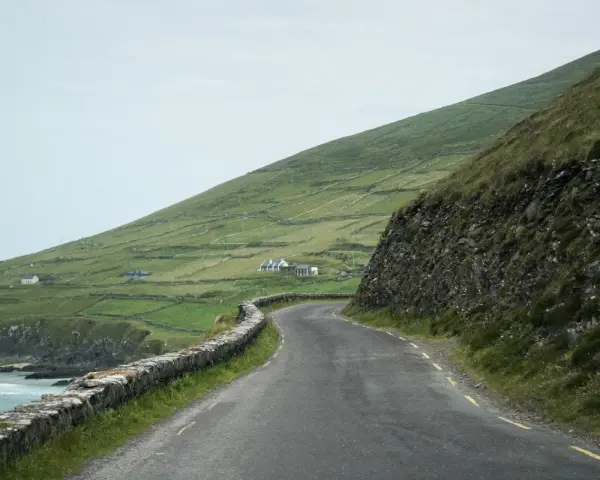 A winding road along the coast of Ireland, perfect for renting a car and exploring the dramatic green hills and stone walls.