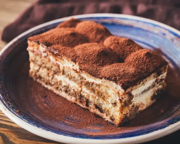 Pyszny kawałek tiramisu z mascarpone, posypany kakao, na niebieskim talerzu. Idealny na deser.