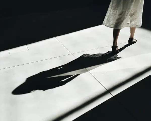 Długa, dramatyczna cień osoby w białej sukience na jasnej posadzce. Jakby zniknęła, zostawiając tylko ślad, niczym w przypadku ghostingu. Co to znaczy?