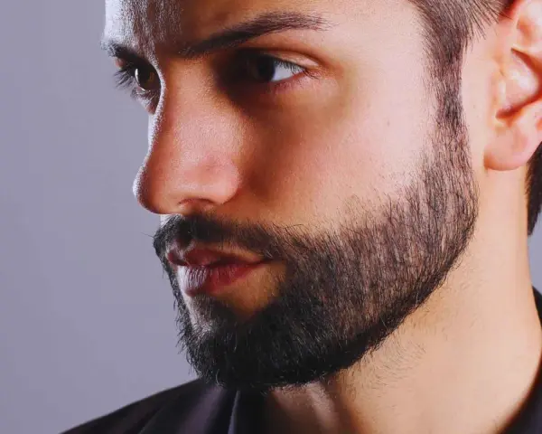 Primer plano de un hombre con barba cuidada, con un estilo fade beard que se difumina hacia las mejillas.