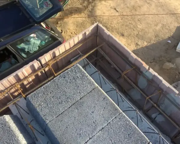 Budowa stropu ackermana w toku. Betonowe pustaki i zbrojenie czekają na zalanie betonem. Obok stoi samochód.