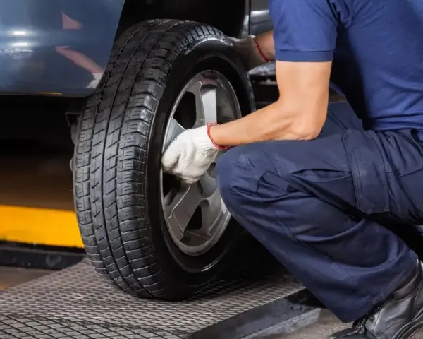 Mechanik w białych rękawiczkach dokręca śruby koła. Czas pomyśleć, kiedy wymienić opony na letnie.