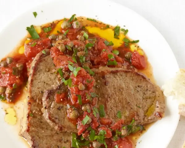 Zwei saftige Scheiben Rindfleisch, bedeckt mit einer würzigen Tomaten-Kapern-Sauce, serviert mit Brot. Ein authentisches Gericht im Stil Pizzaiola original italienisch.