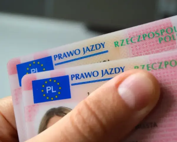 Dłoń trzyma polskie prawa jazdy. Widoczne napisy "PRAWO JAZDY" i "RZECZPOSPOLITA POLSKA" sugerują różne kategorie prawa jazdy.