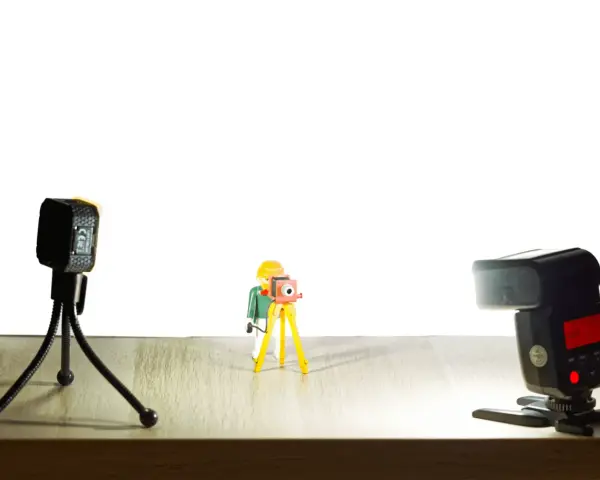 Une figurine Playmobil prend une photo avec un appareil sur trépied. Une autre caméra et un flash sont présents. Vue macro.