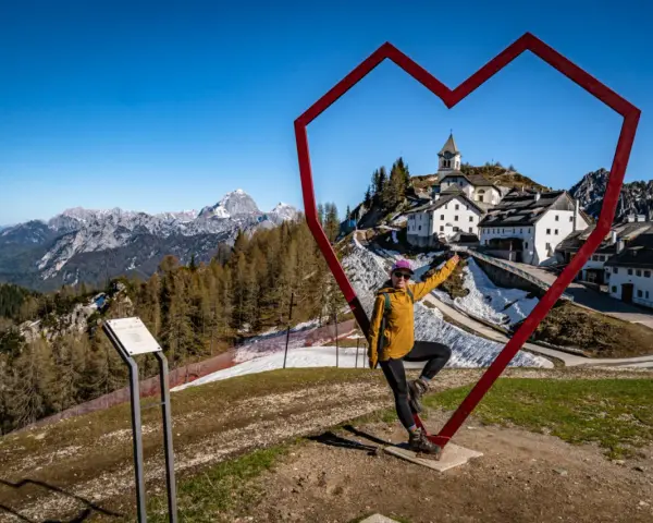Kobieta w sercu z widokiem na górską wioskę Monte Lussari.