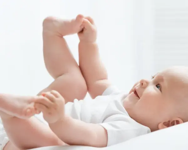 Uśmiechnięte dziecko leży na plecach, podnosząc nóżki. Czas na zmianę pampersów na większe, gdy maluch rośnie.