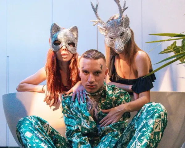Smolasty z dużymi oczami w otoczeniu dwóch kobiet w błyszczących maskach.