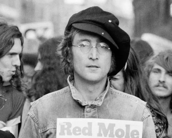 John Lennon w czapce i okularach, trzymający plakat "Red Mole". W tle inni ludzie, być może fani jego utworów.