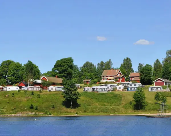 Gröna kullar med husbilar och röda stugor vid en sjö. En idyllisk plats för greans camping.