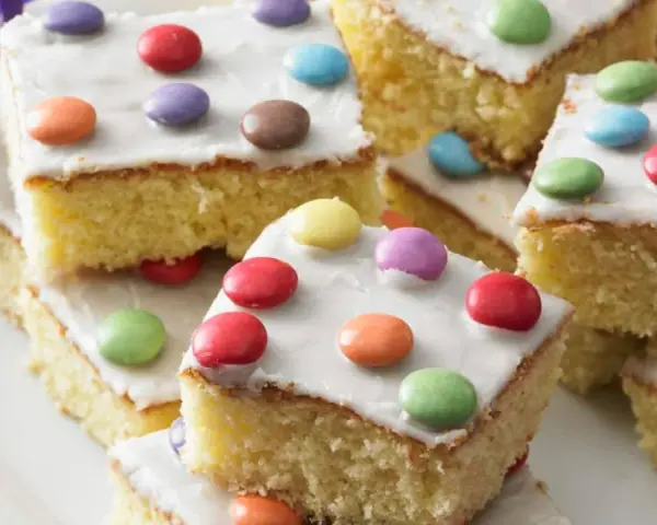 Bunter Fantakuchen-Rezept: saftige Kuchenstücke mit weißer Glasur und bunten Smarties. Perfekt für Kindergeburtstage!