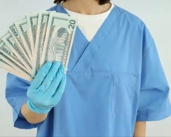 Osoba w niebieskim fartuchu i rękawiczkach trzyma wachlarz banknotów 20 dolarowych.