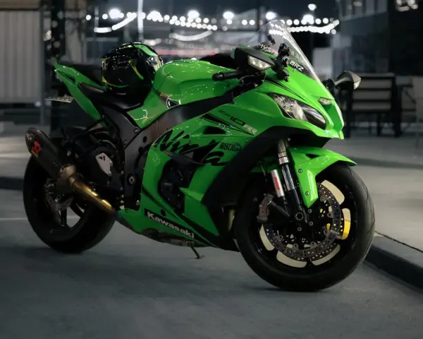 Japoński motocykl Kawasaki Ninja ZX-10R w jaskrawym zielonym kolorze, z kaskiem na siedzeniu, gotowy do nocnej jazdy.