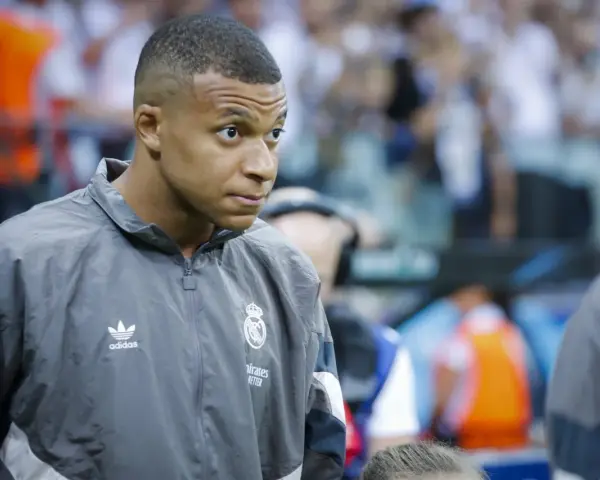 Kylian Mbappé w szarej kurtce z logo Realu Madryt, gotowy do gry.
