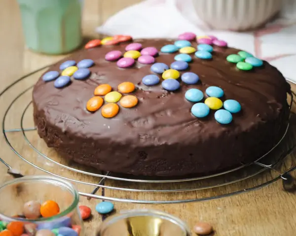 Schokokuchen mit bunten Smarties, perfekt für Kinder. Ein Glas mit weiteren Süßigkeiten steht daneben.