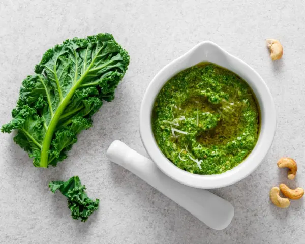 Pesto z jarmużu do słoika, gotowe do przechowywania. Obok liść jarmużu i orzechy nerkowca.