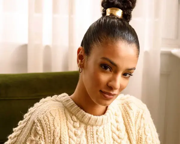 Donna con una coda alta cerimonia, indossa un maglione in maglia color crema e orecchini a cerchio dorati.