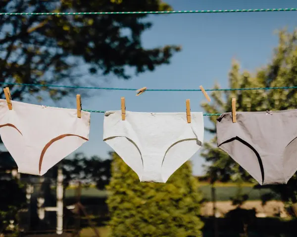 Drei Unterhosen in verschiedenen Grautönen trocknen an einer Wäscheleine. Das Bild zeigt den Prozess des Unterhosen waschen.