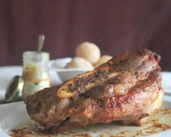 Costilla de ternera asada jugosa con hueso, servida en plato blanco con salsa y guarnición.