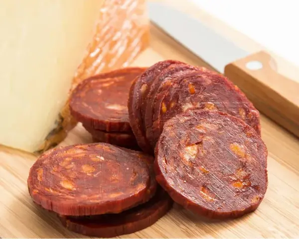 Plasterki pikantnego chorizo, kawałek sera i nóż na desce. Idealne na przekąskę, zastanawiasz się chorizo co to?