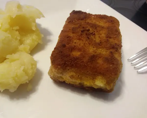 Chrupiąca panierowana kostka rybna z purée ziemniaczanym na białym talerzu.